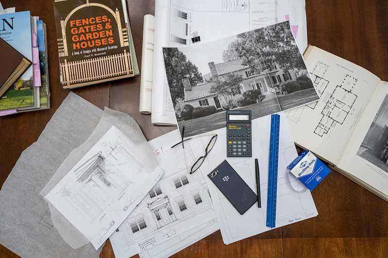 Architecture book, sketches, glasses, a pen and ruler, and other items lay on a wooden desk.