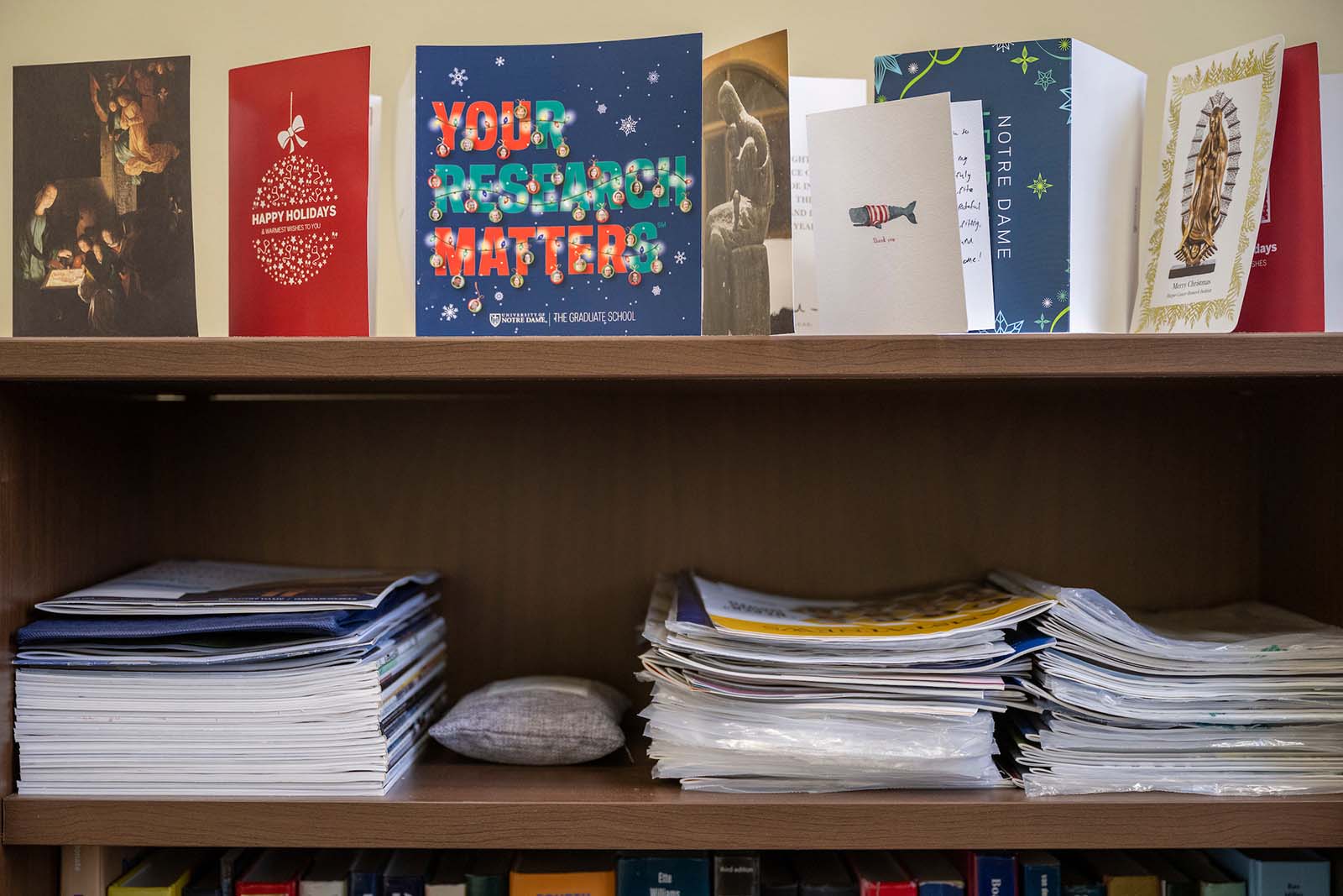 A shelf with stacks of papers and magazines, and holiday cards displayed at the top.